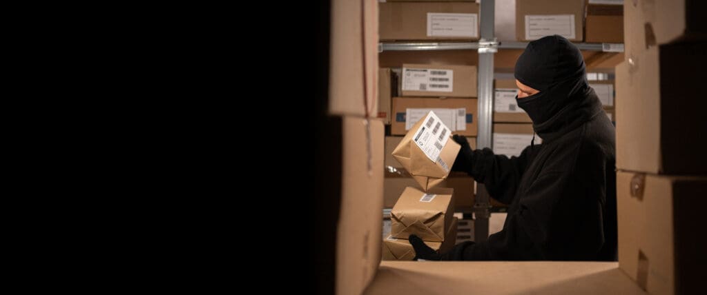  Masked thief stealing parcels from an unsecured apartment mailroom, highlighting the need for Smart Package Room security solutions in multifamily properties.