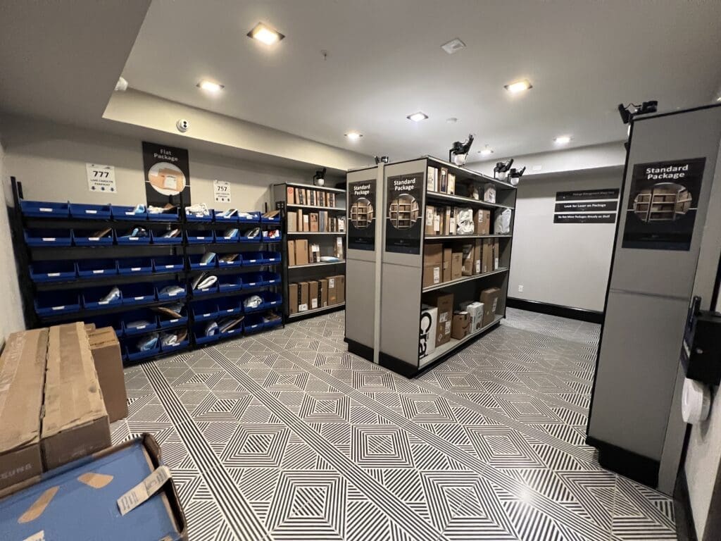 The Smart Package Room system with open shelving, categorized bins, and computer vision cameras with laser guidance managing packages of all sizes in a multifamily apartment building.