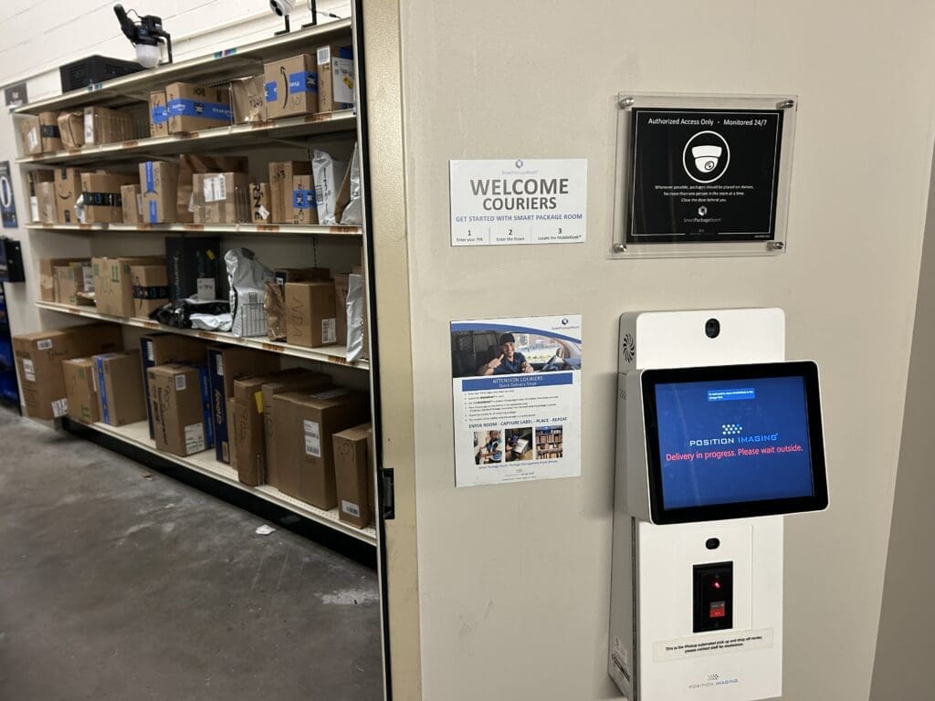 Smart Package Room with open shelving filled with delivered parcels, a courier check-in kiosk displaying Position Imaging’s interface, and signage indicating 24/7 monitored, authorized access, illustrating a secure, automated package management solution.