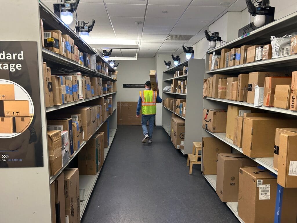 Courier delivering parcels to open shelving in a Smart Package Room equipped with computer vision technology, showcasing advanced package management solutions for multifamily properties.

