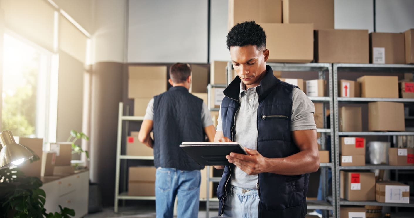 IMG_5127 Multifamily staff organizing shelves of packages and reviewing a tablet, illustrating mailroom organization ideas that improve efficiency in apartment buildings.